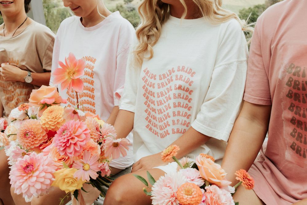 Close-up of matching t-shirts and coral pink floral bouquets in group setting.