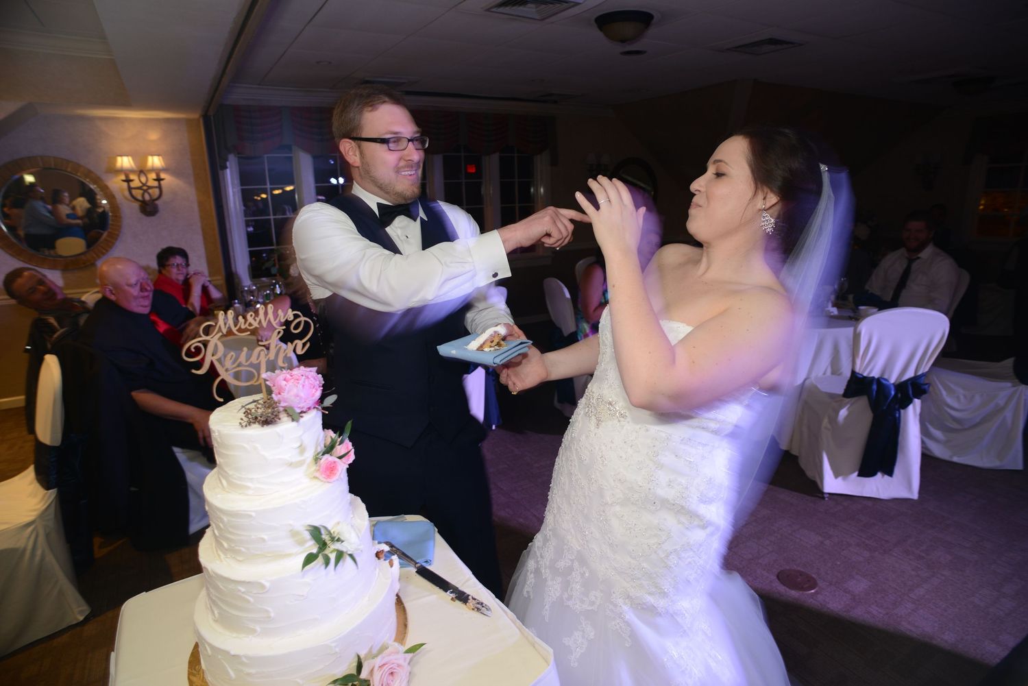 Couple shares playful moment while cutting their white tiered wedding cake.