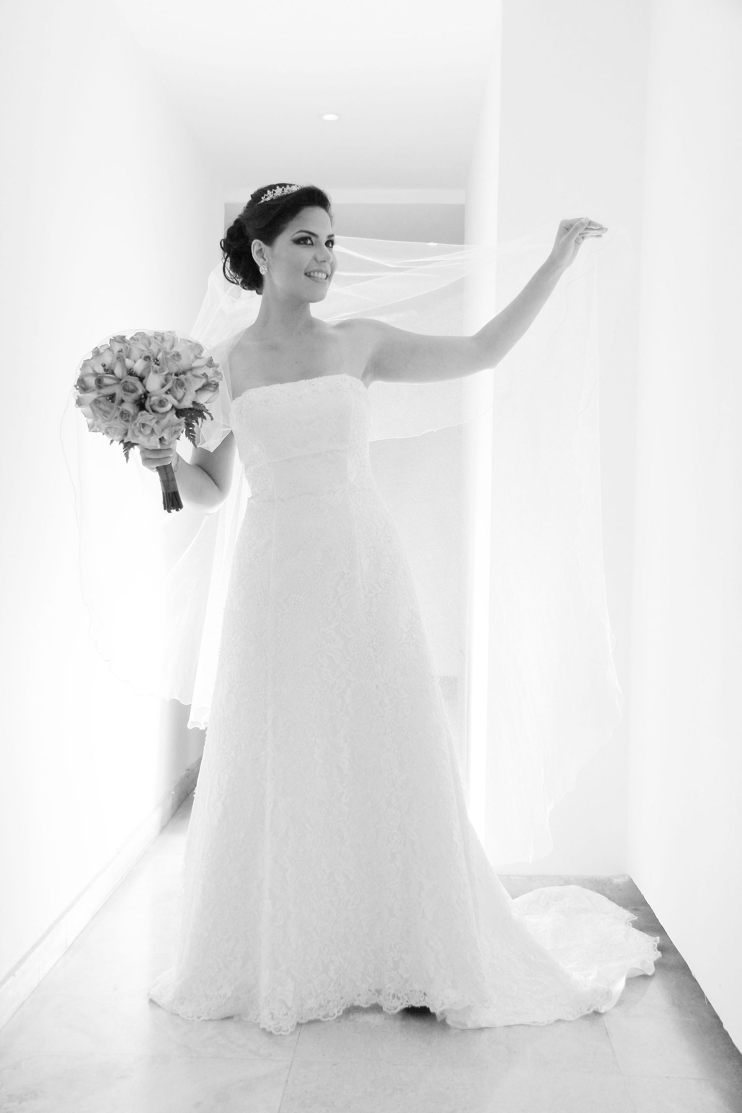 A bride in a classic white strapless gown holds a bouquet while posing against a light background.