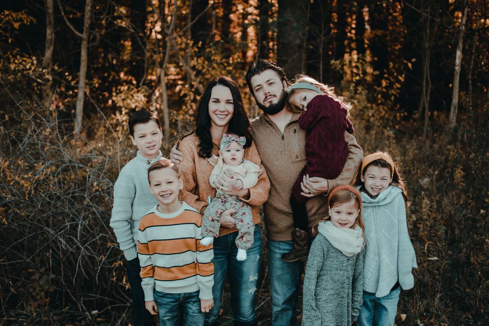 Large family of seven with five children posing together in golden autumn forest for fall family photos.