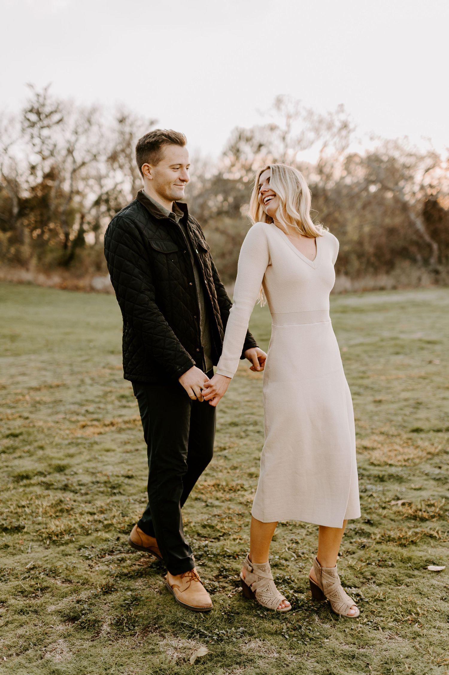 Romantic couple stands in a field at sunset wearing coordinated cream and black outfits.
