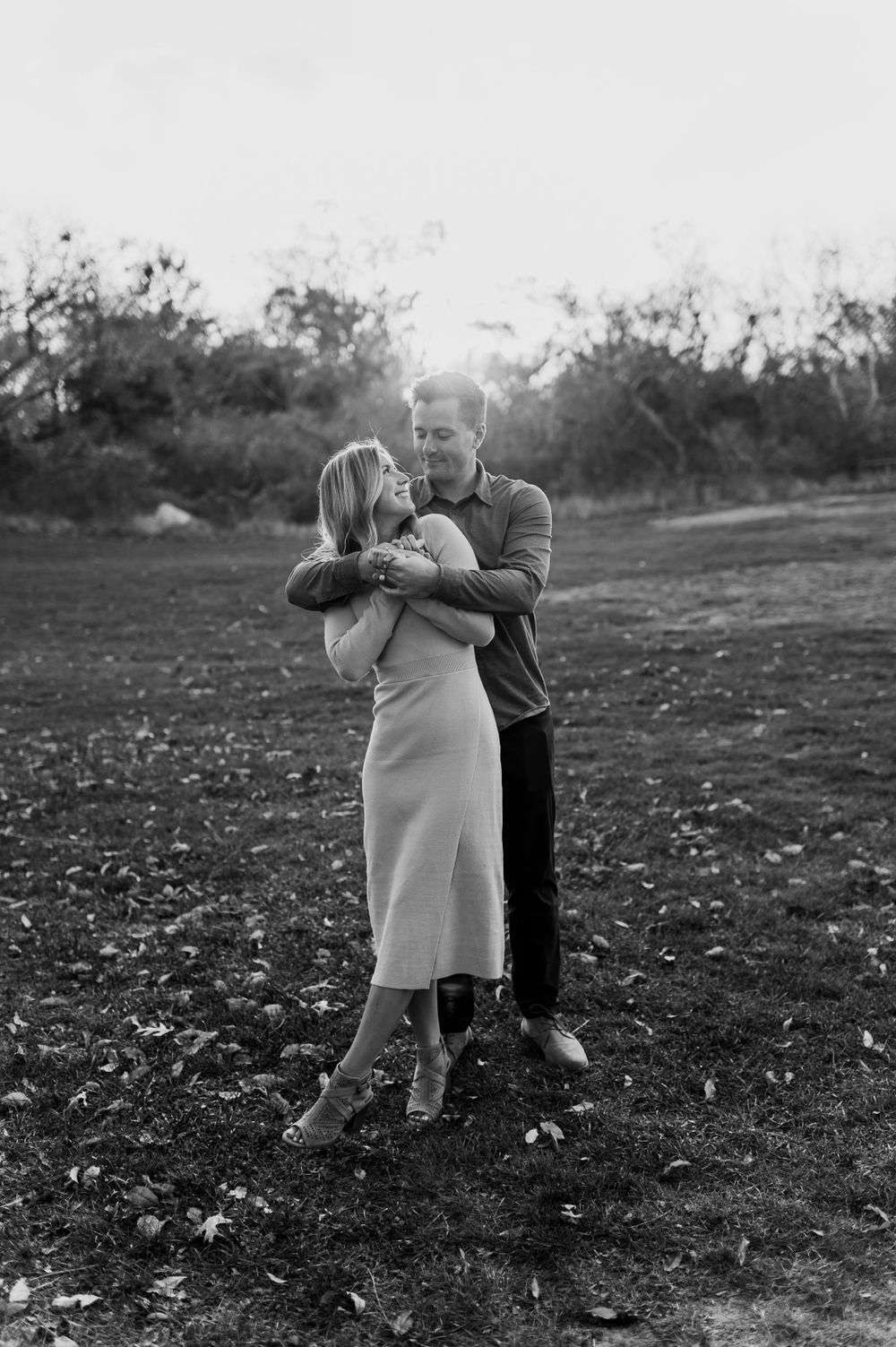 Black and white photo of couple playing in field during sunset.