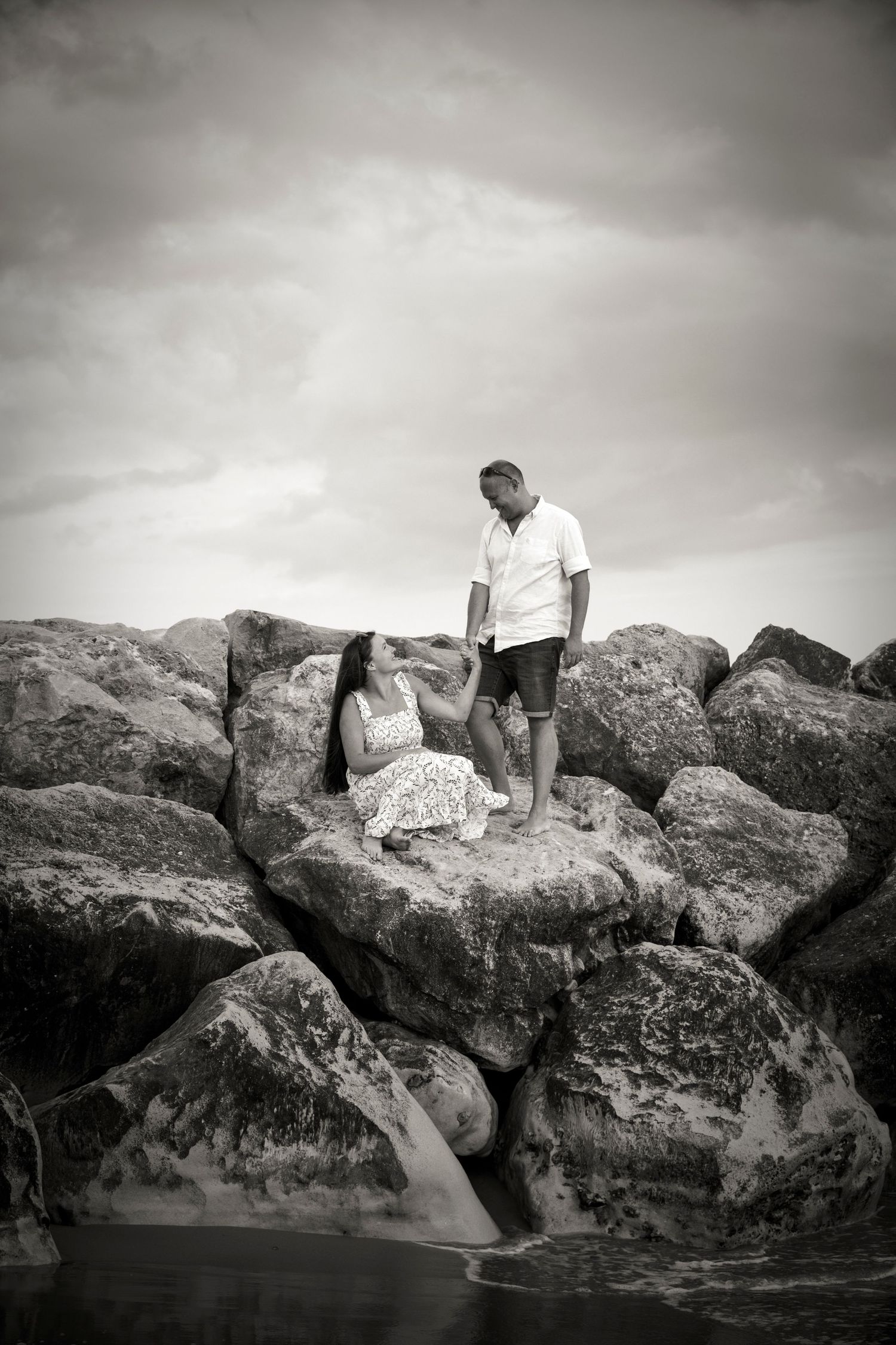 A black and white photo captures two people exploring rocky coastal formations.