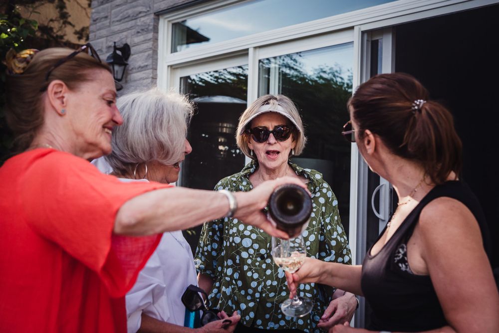 Colour image of a group of mature women chatting together as one pours champagne into a glass for another.