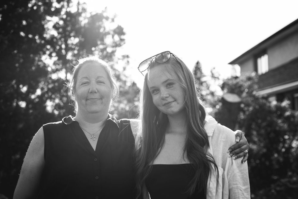 BW image of a woman standing beside her teenage daughter with the sun shining behind them.