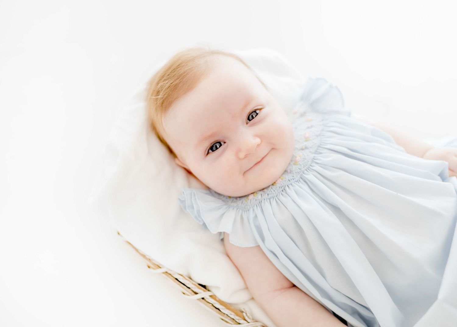 Baby in light blue dress lying on white backdrop during studio portrait session.
