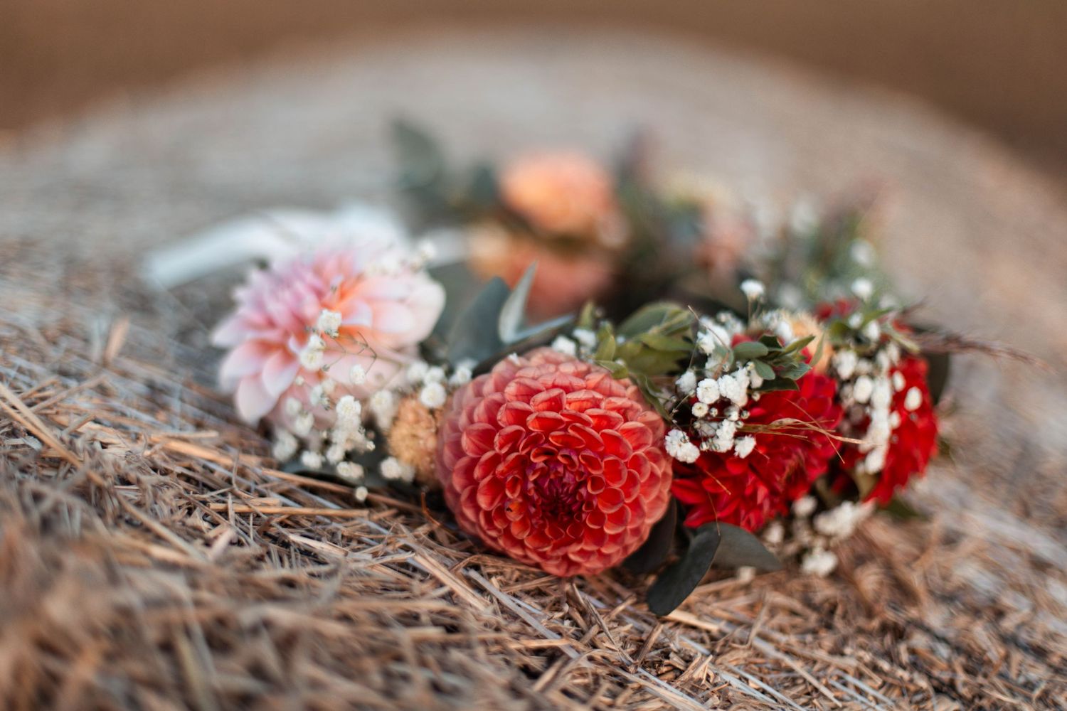 Close-up of vibrant red dahlia and baby's breath flower crown resting on rustic woven surface.