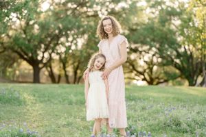 Mother and daughter in matching dresses embrace in sunlit garden setting.