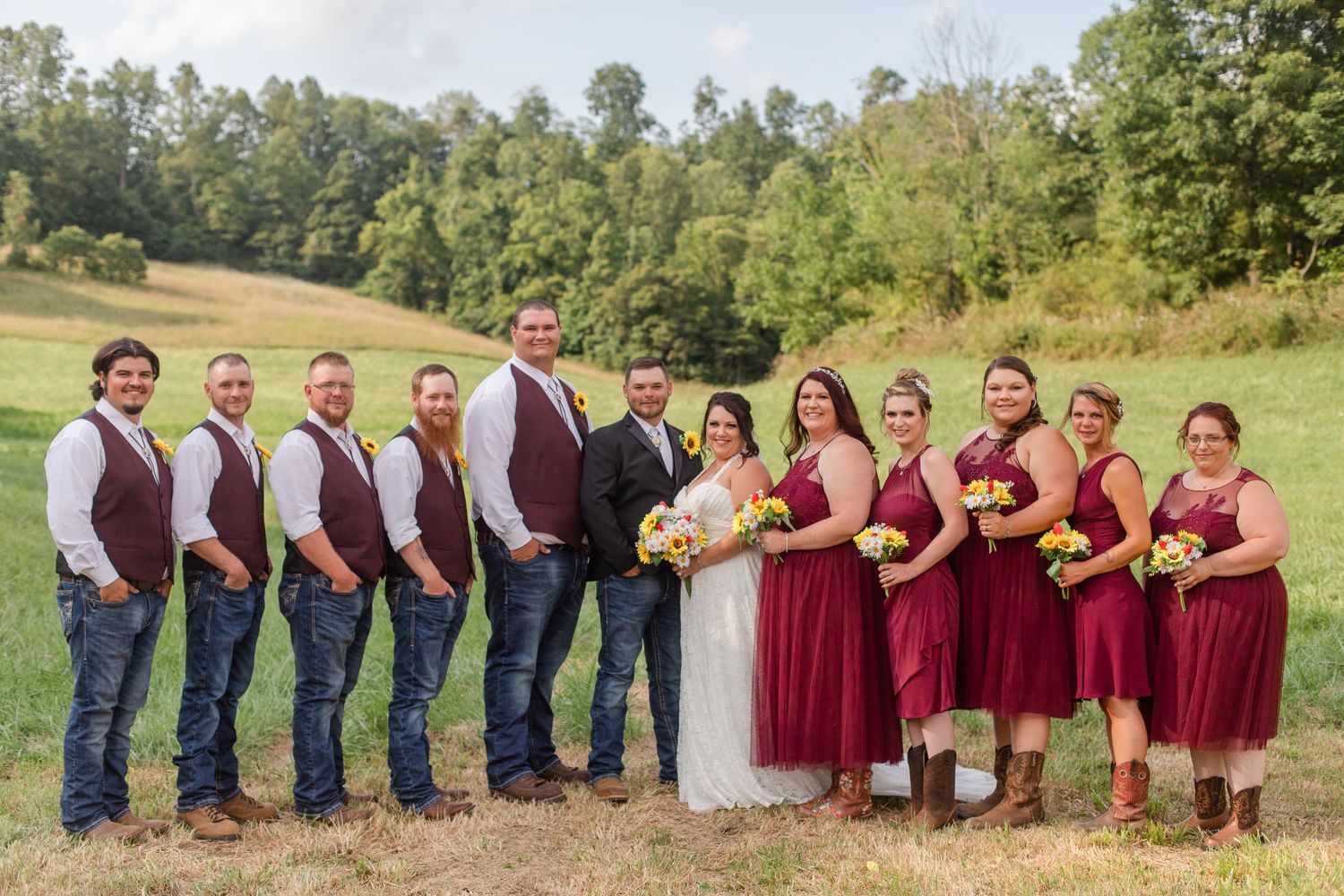 Wedding party in burgundy and navy attire posed together in a rustic outdoor setting.