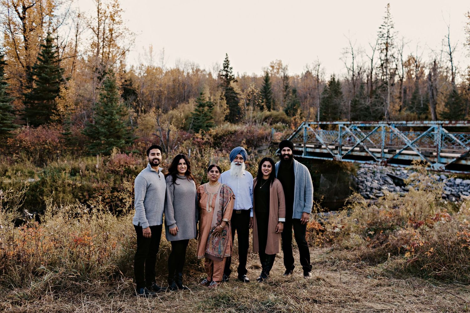 A group stands outdoors in front of an autumn landscape with a bridge structure visible in the background.