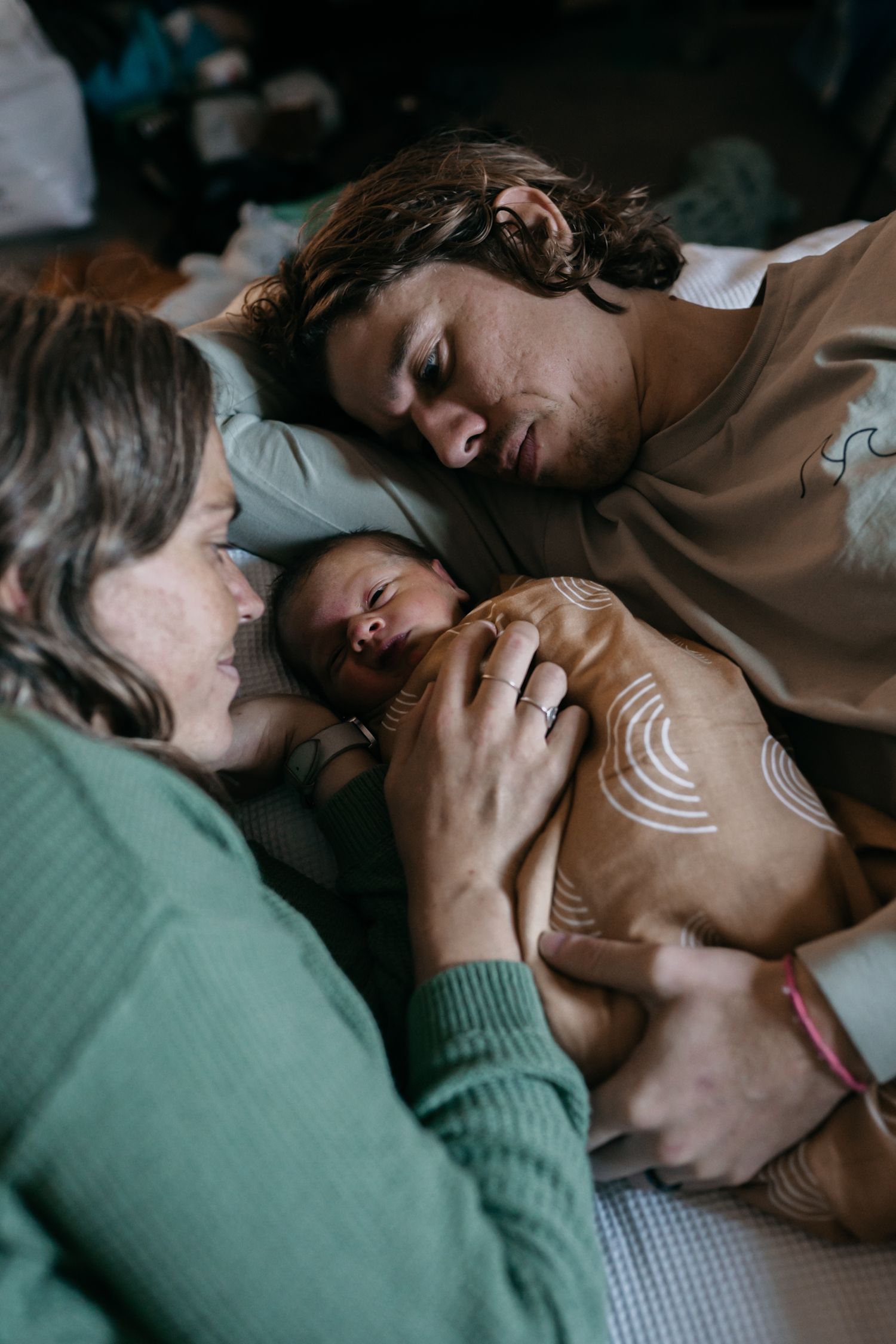 A mum and dad lying on a bed with their newborn baby during a newborn family session in Perth