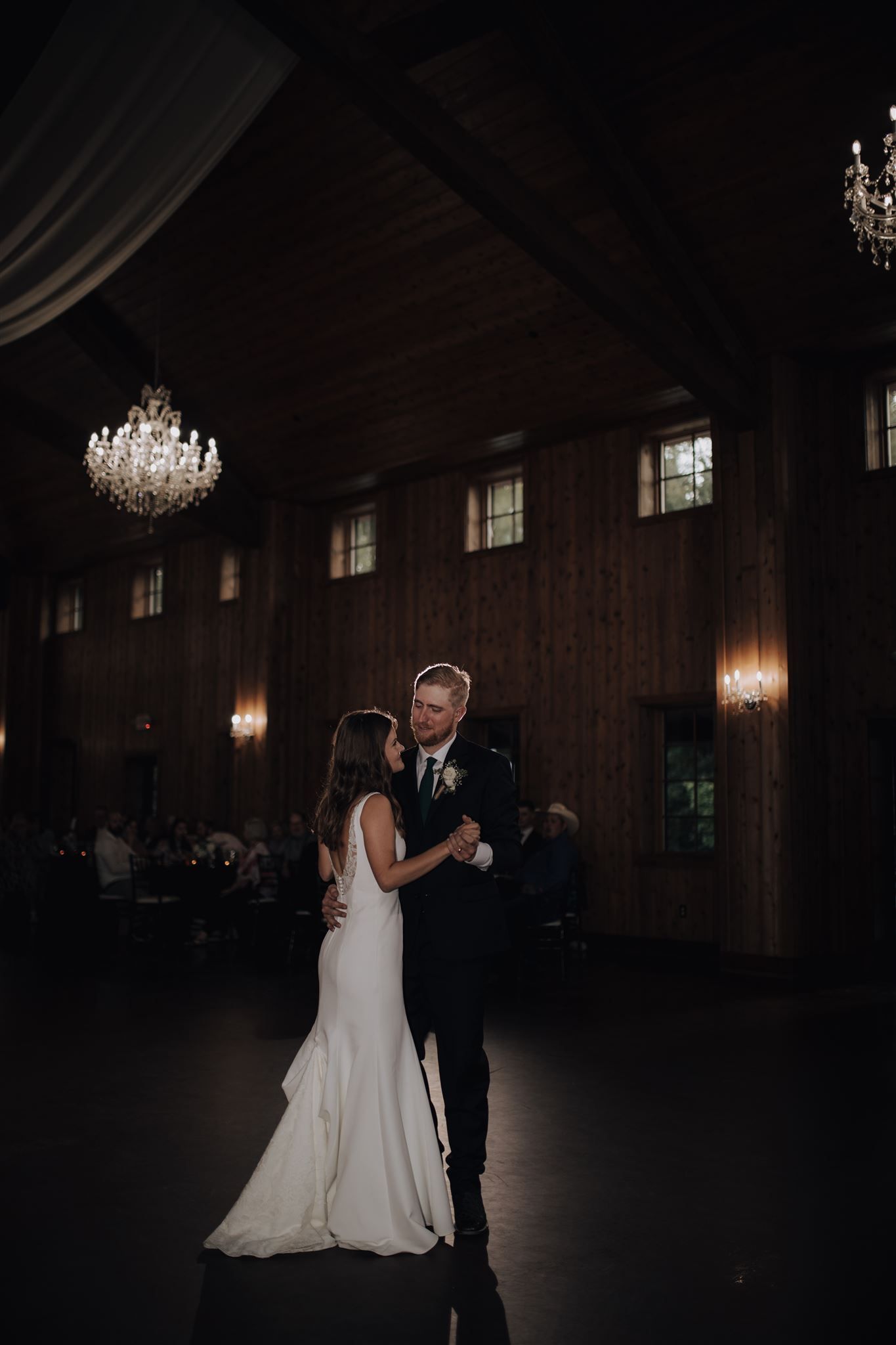 First dance moment captured in dark reception hall with sparkling chandeliers above.