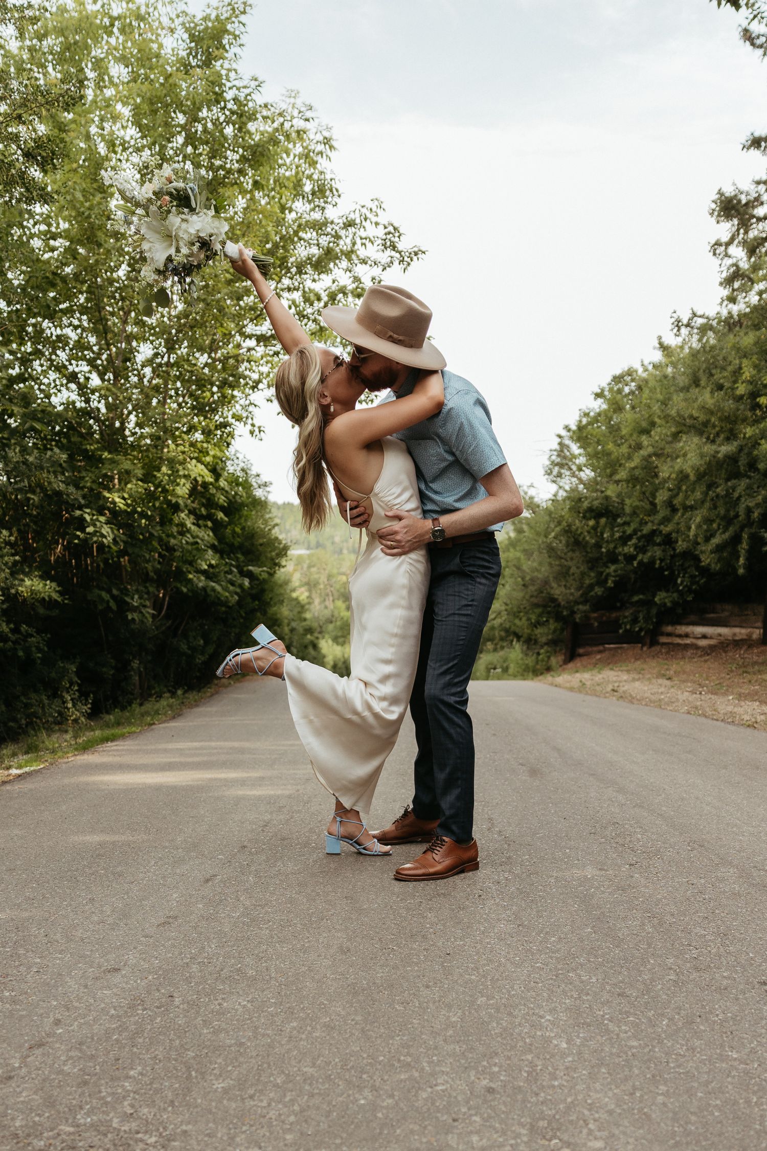 A romantic dance dip pose on a paved pathway surrounded by trees.