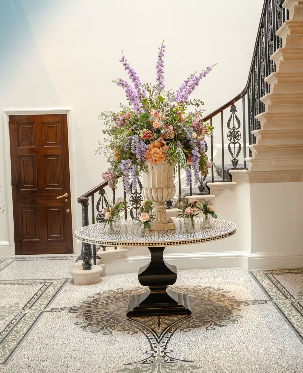 Decorative floral arrangements in black urns line a grand hallway with marble floors.
