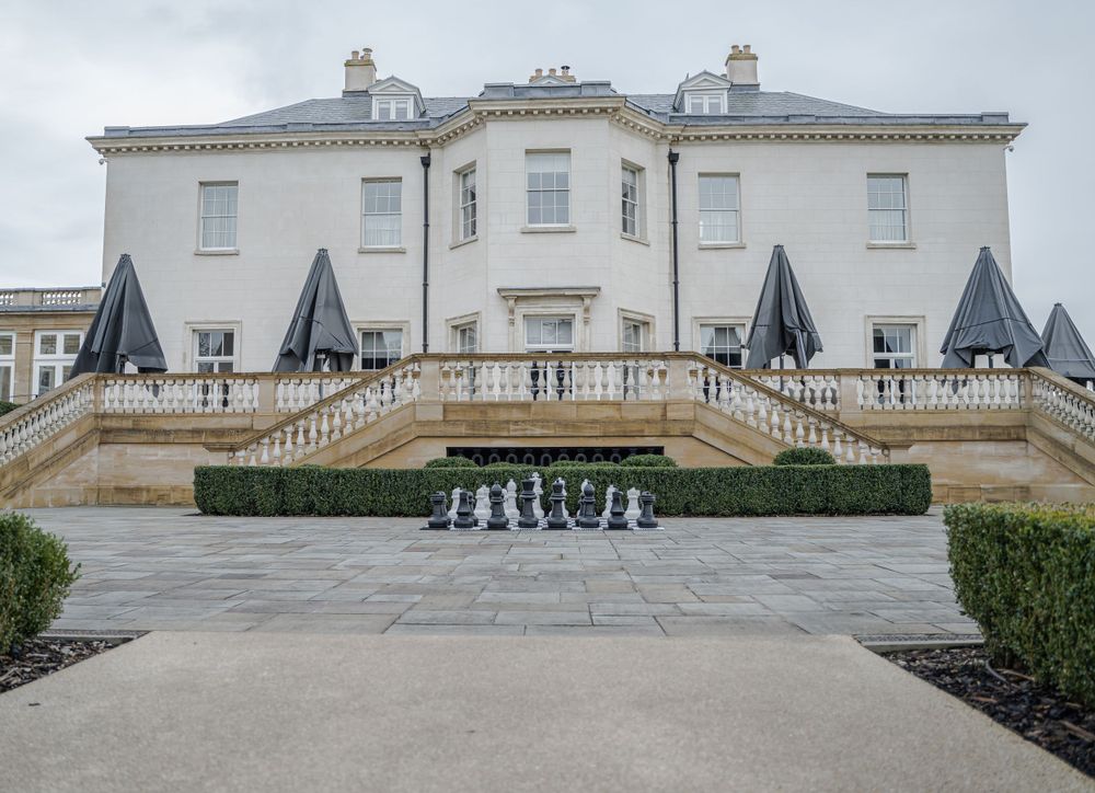 Exterior view of a grand white manor house with classical architecture and manicured grounds.