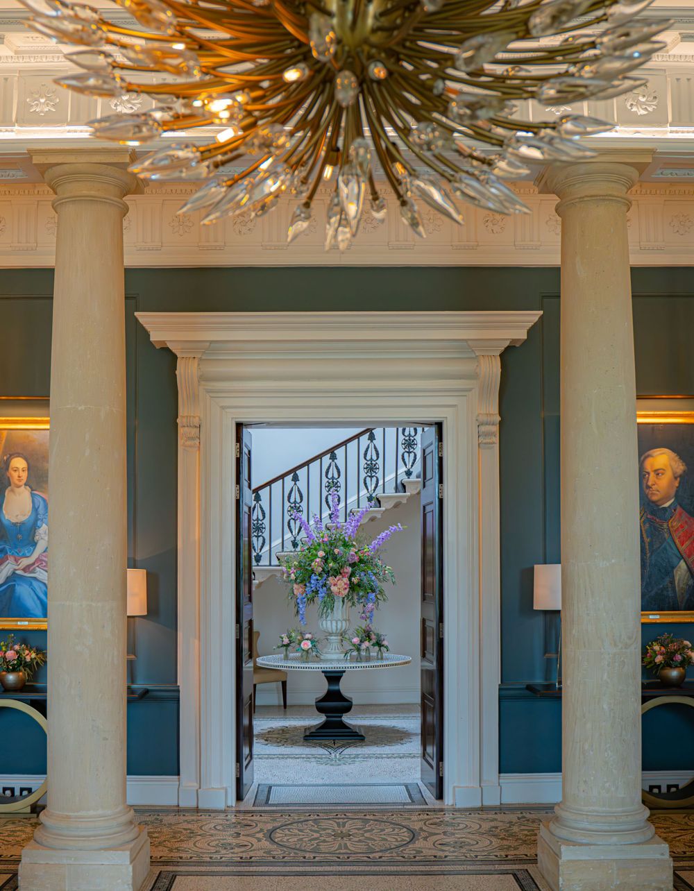 Grand interior hallway with ornate gold chandeliers and classical columns featuring modern art displays.