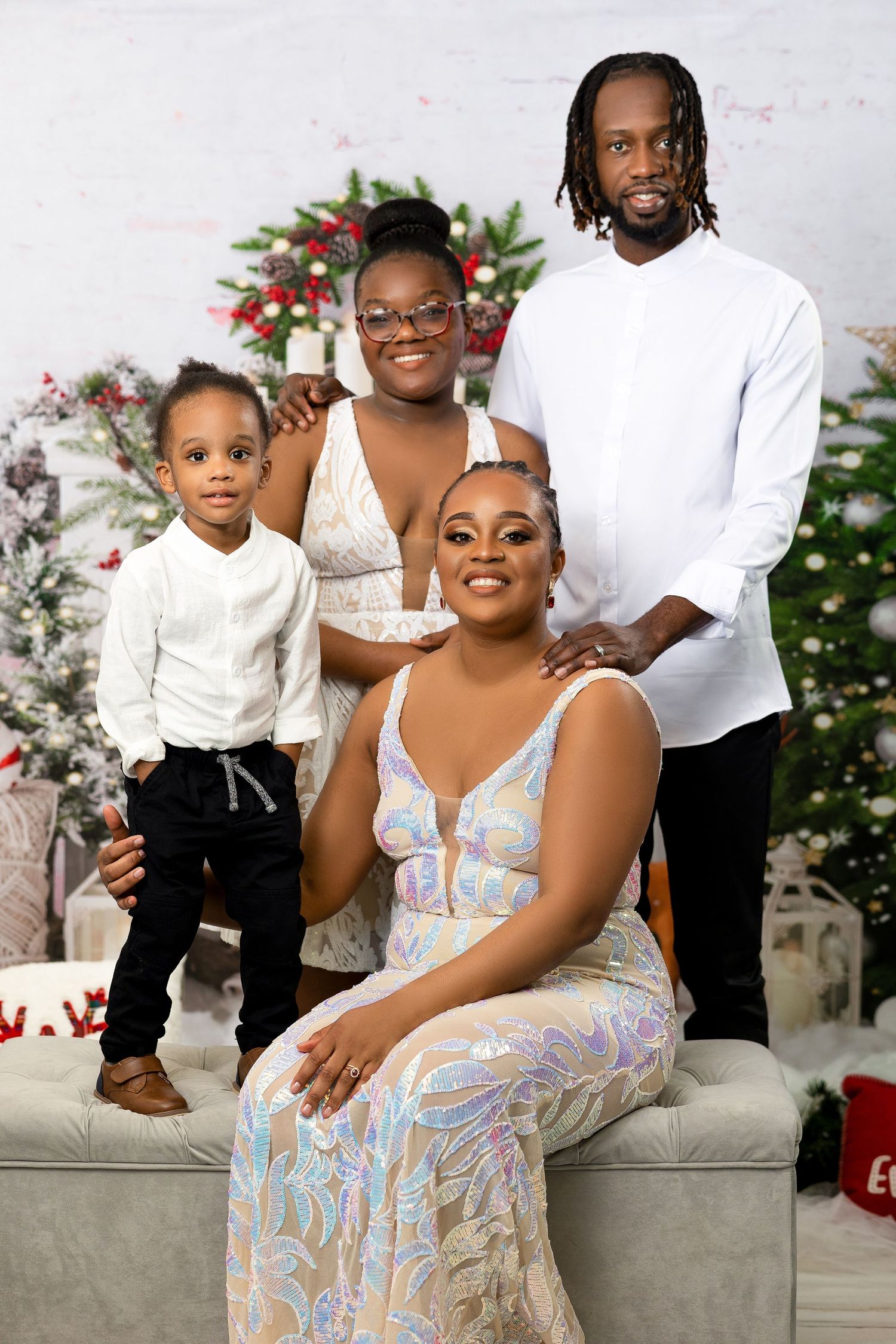 Family of four posing in elegant holiday attire in front of a decorated Christmas tree backdrop.