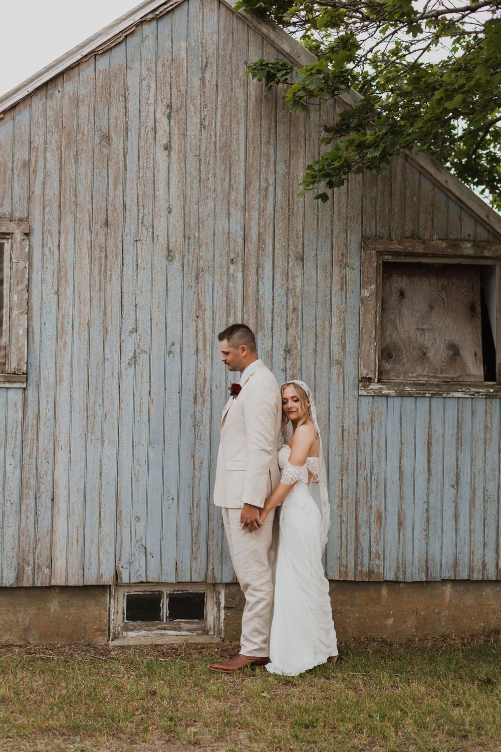 Rustic barn wedding portrait with couple standing against weathered blue wooden siding.