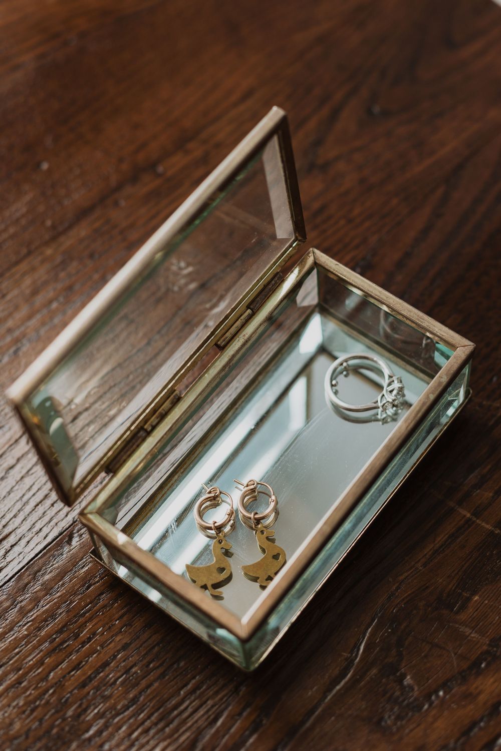 Wedding rings and jewelry displayed in clear glass box on wooden surface.