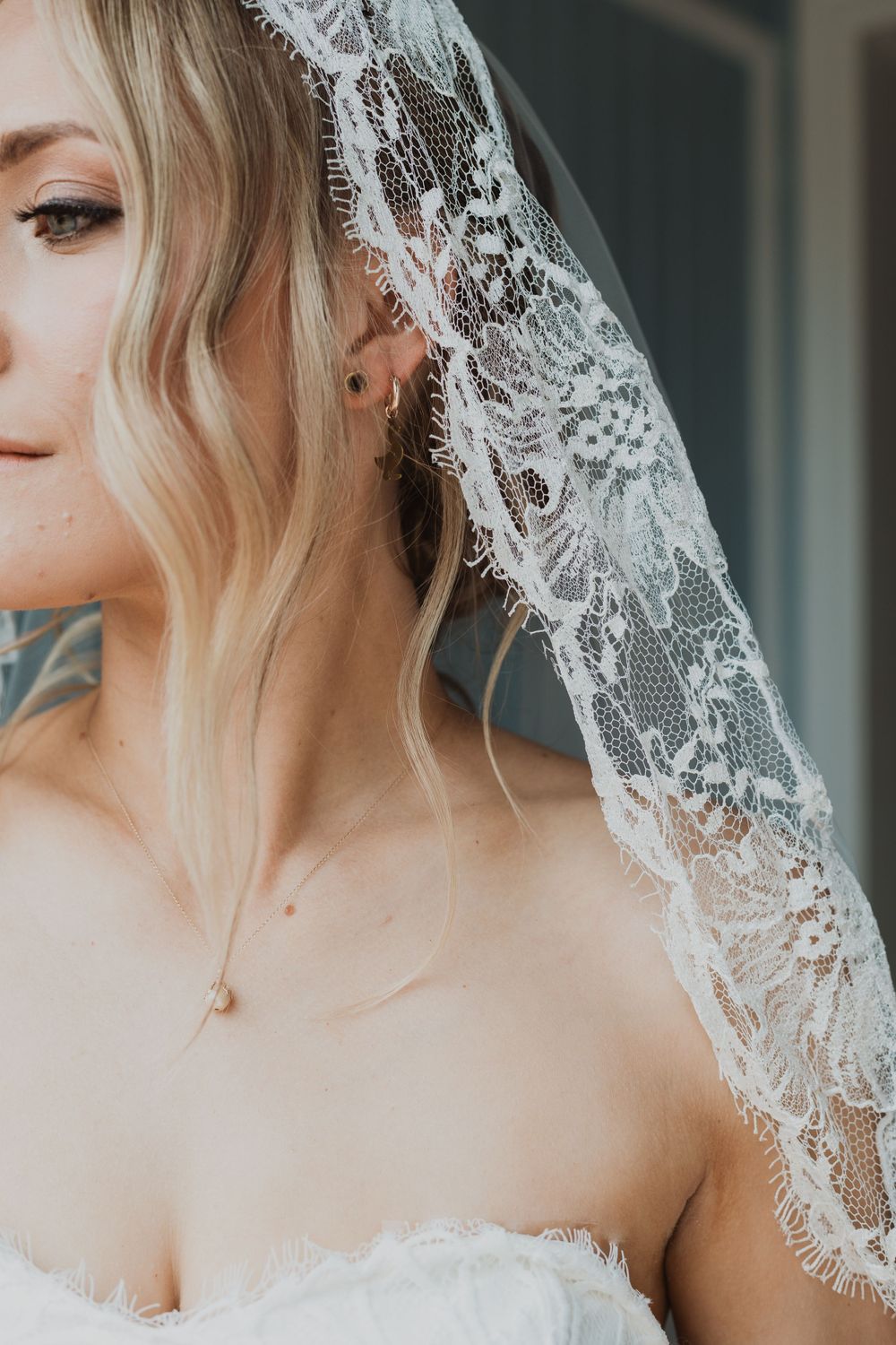 Delicate white lace veil drapes elegantly over a bride wearing a strapless wedding dress.