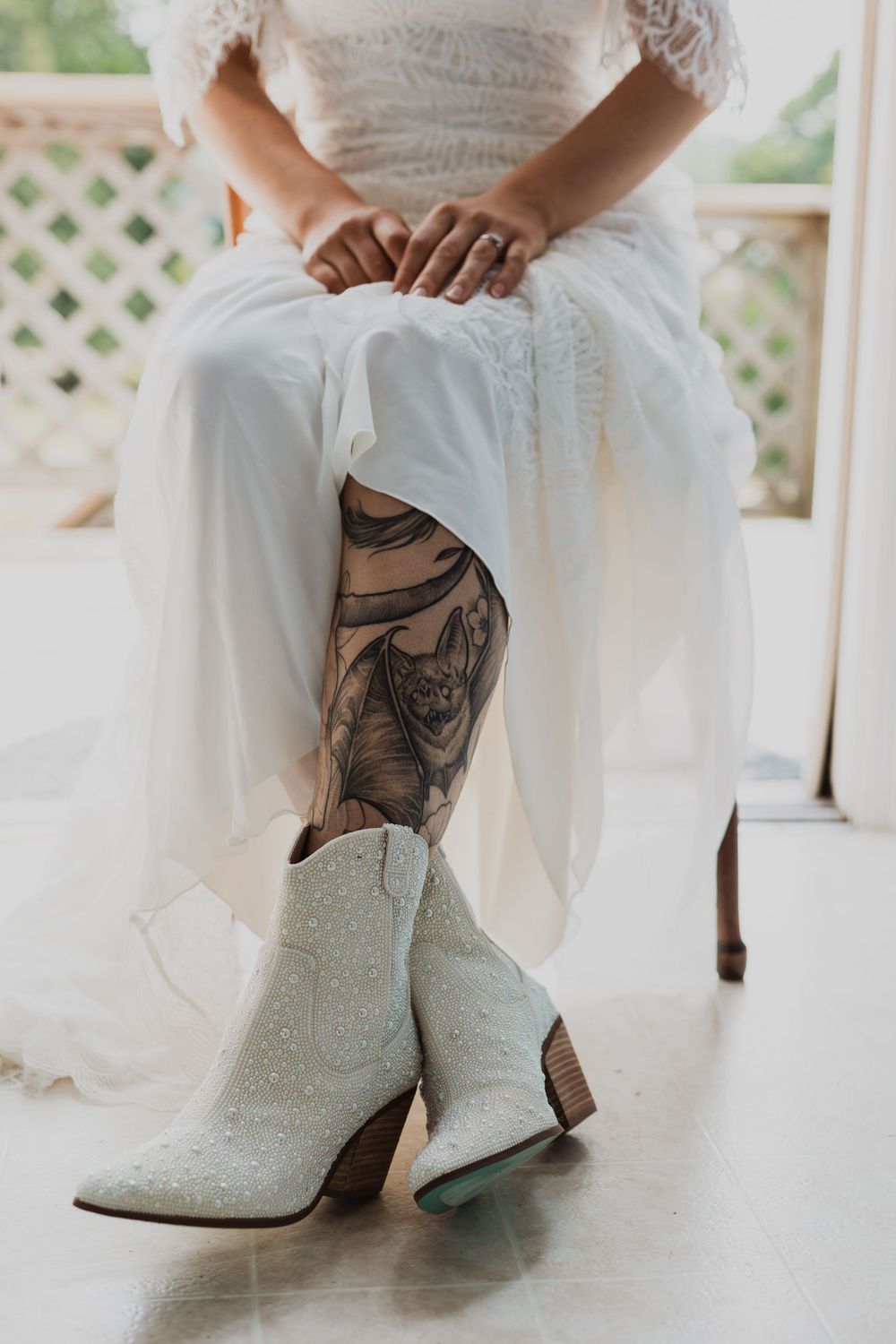 White cowboy boots and leg tattoo detail shown beneath a flowing wedding dress hem.