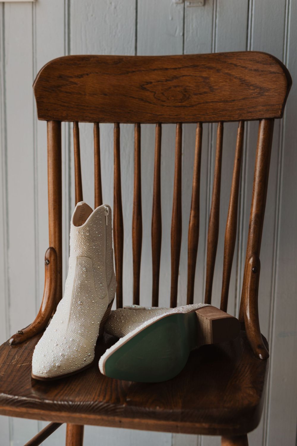 White sparkly wedding boots sitting on wooden Windsor chair.