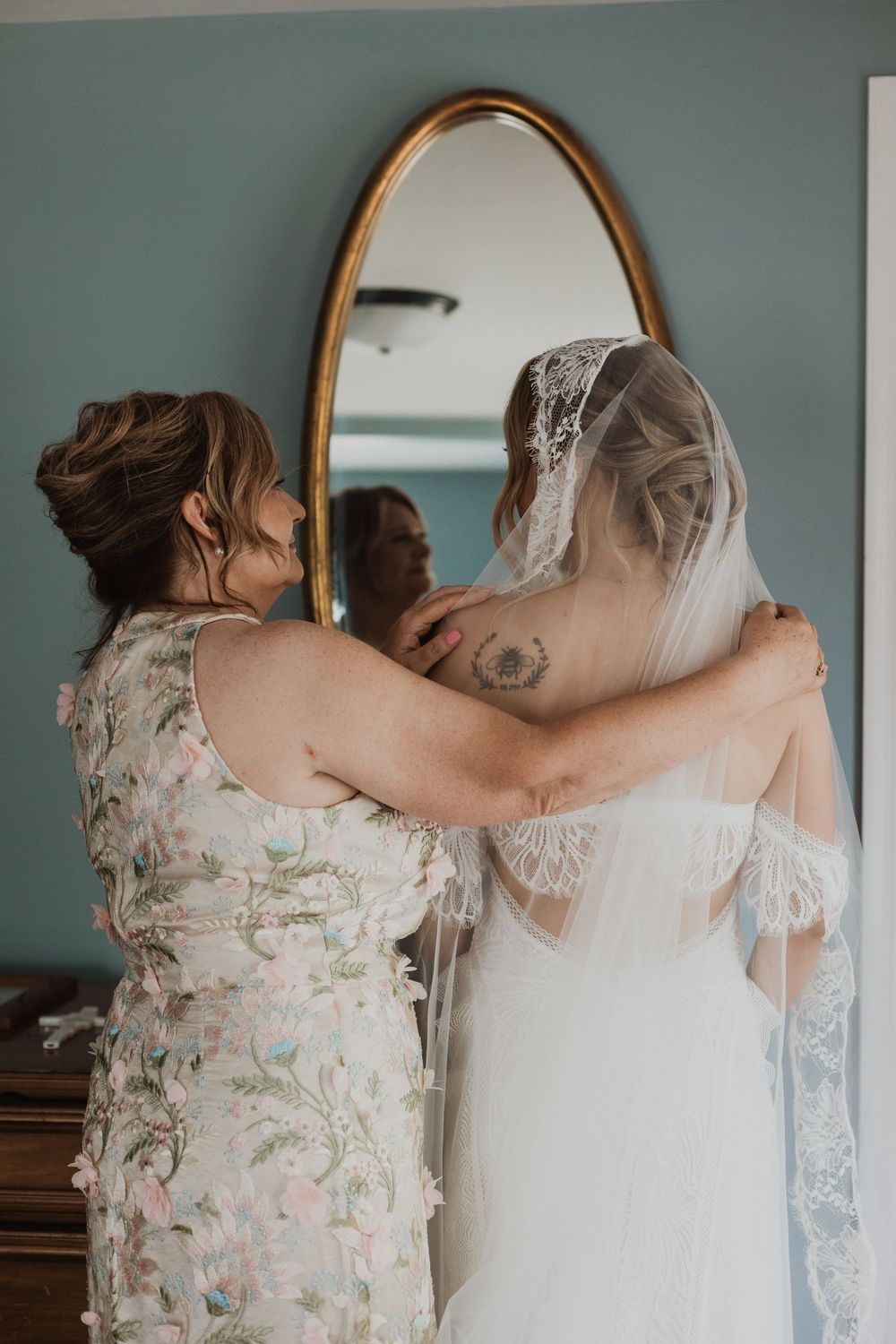 A touching moment as two women embrace in front of an oval mirror during wedding preparations.