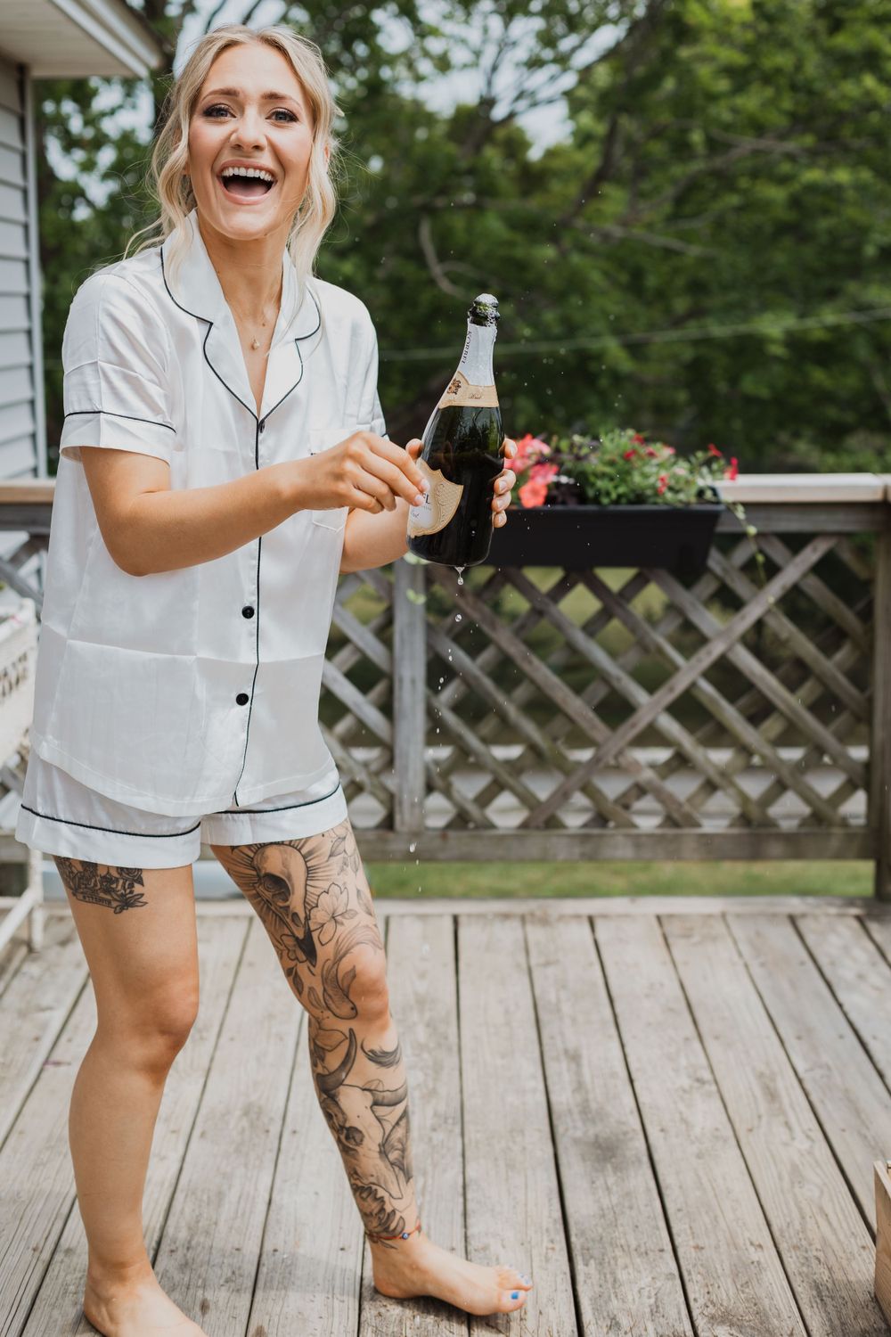 Woman in pajamas enjoying a drink on outdoor deck with lattice fence and flowers.