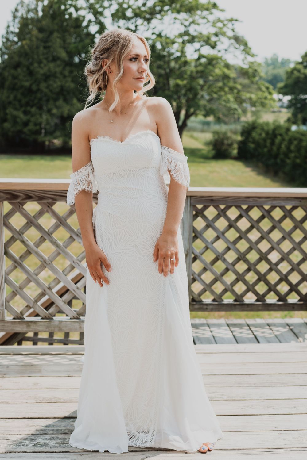 An elegant off-shoulder lace wedding dress with delicate details shown on an outdoor deck.