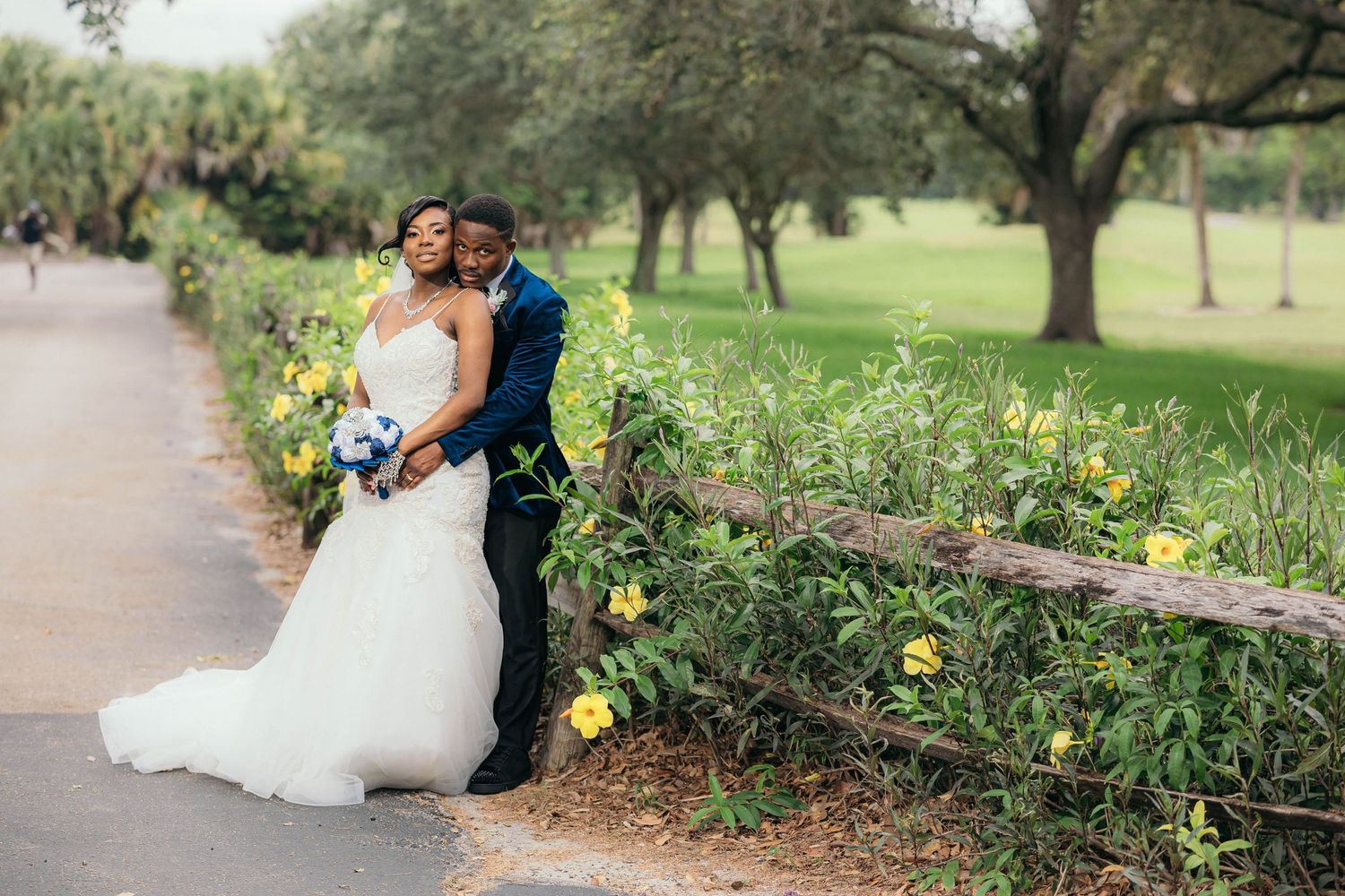 Romantic bride and groom embracing by rustic fence with yellow wildflowers in scenic park.