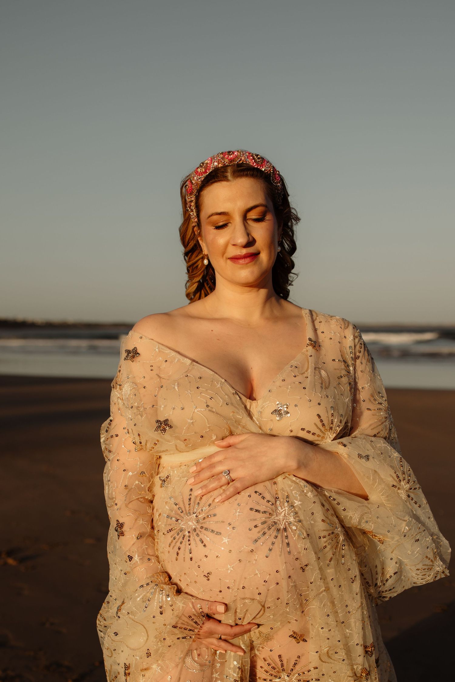 Maternity portrait at sunset on beach in sparkly dress.