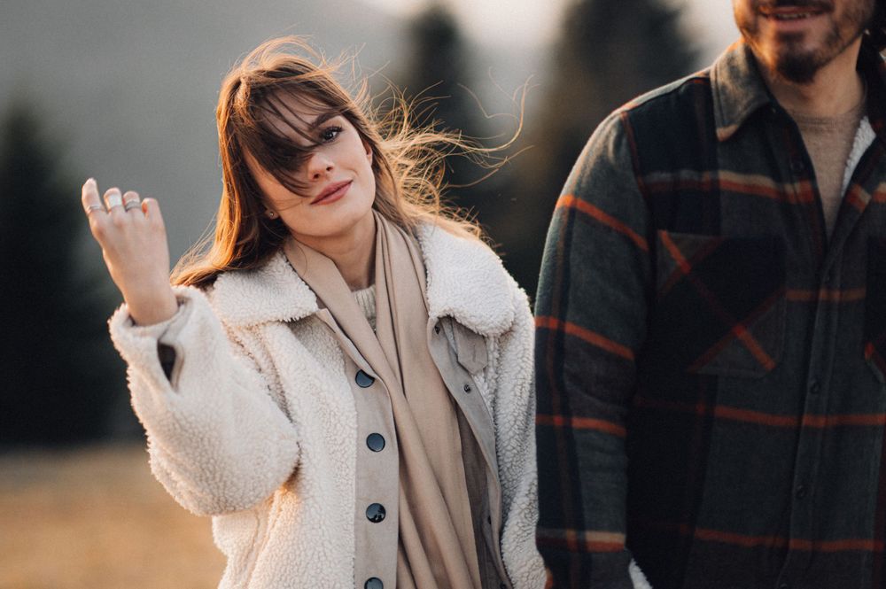 A person in a white coat waving while standing outdoors during golden hour.