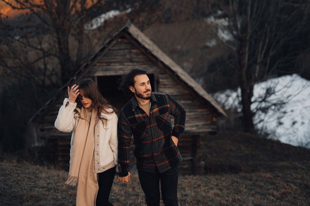 Couple enjoying winter day near old rustic barn in snow.