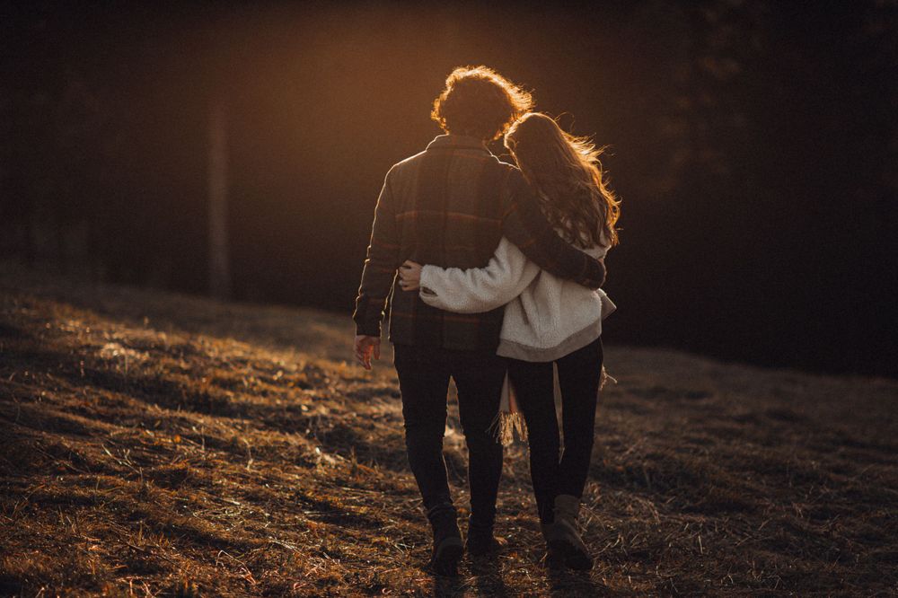 Silhouetted couple walking together against golden sunset on hillside.