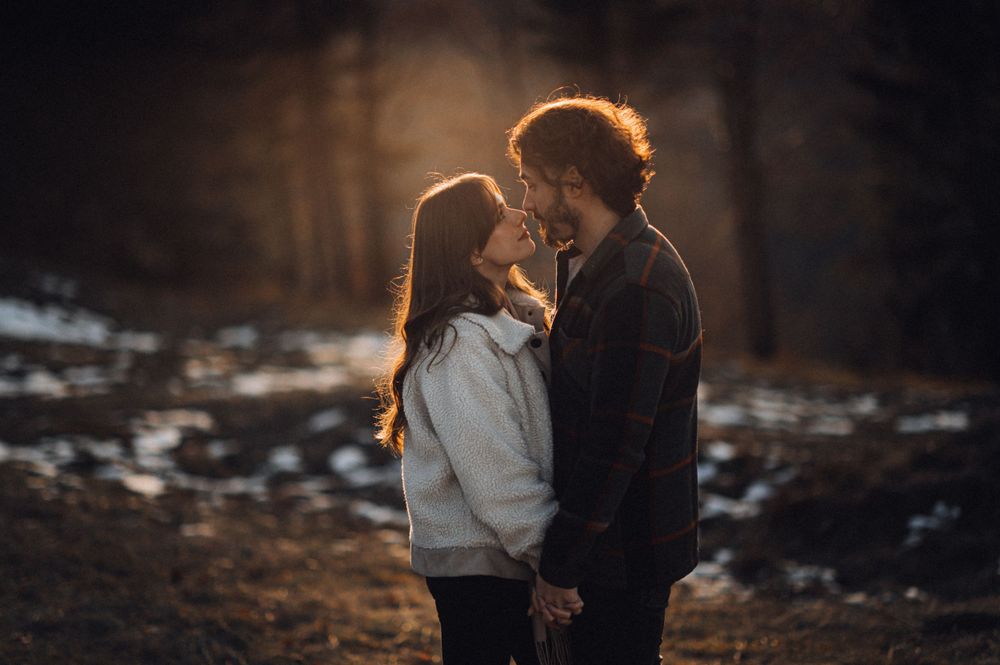 Atmospheric backlit silhouette of a couple embracing in a snowy winter landscape at sunset.