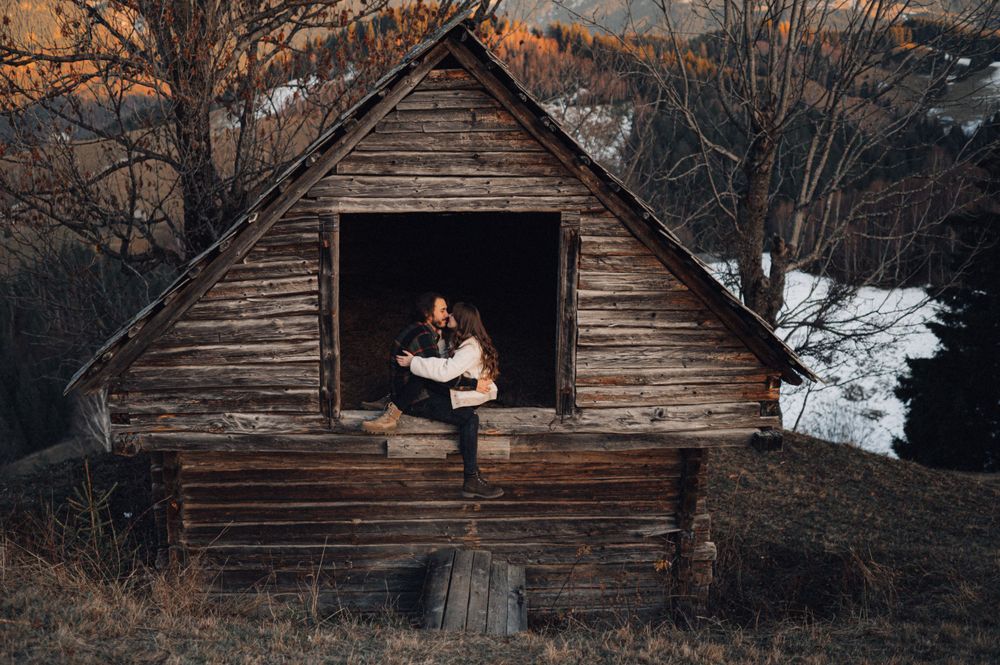 Couple sharing intimate moment in rustic cabin doorway with snowy mountain backdrop.