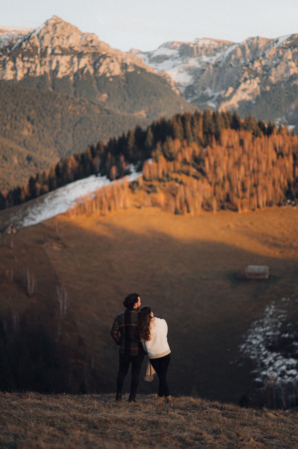 A couple admires mountain views at sunset from a scenic hilltop overlook in winter.