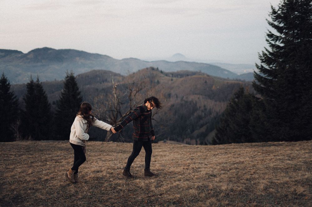 Playful couple dancing together on hilltop with mountain landscape in background.