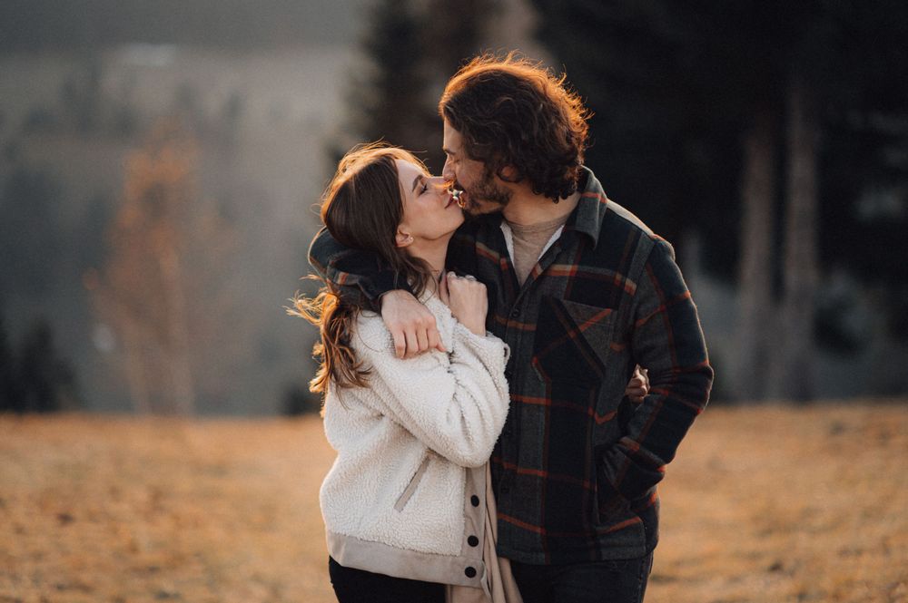 A couple shares an intimate embrace against a backdrop of misty mountains and pine trees.
