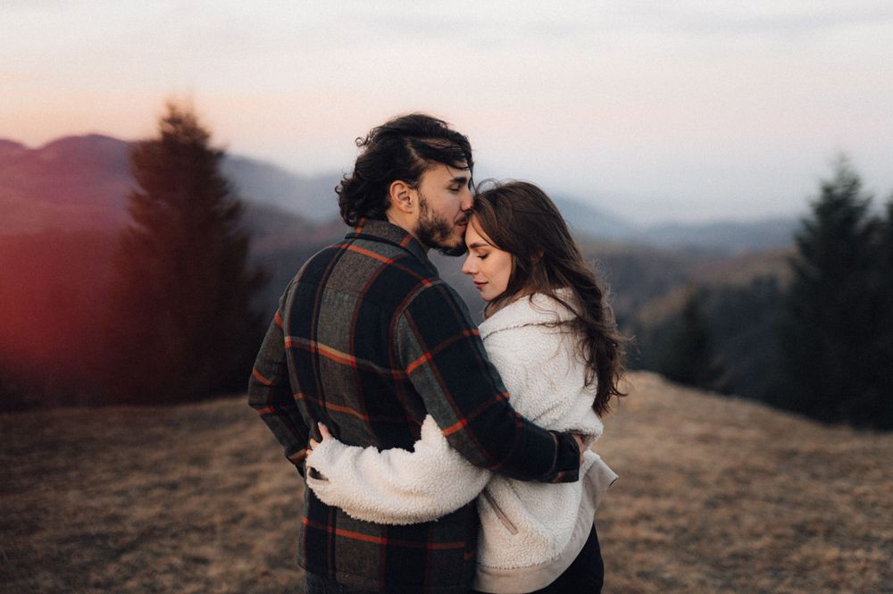 A romantic embrace captured at sunset with mountains and trees silhouetted in the background.