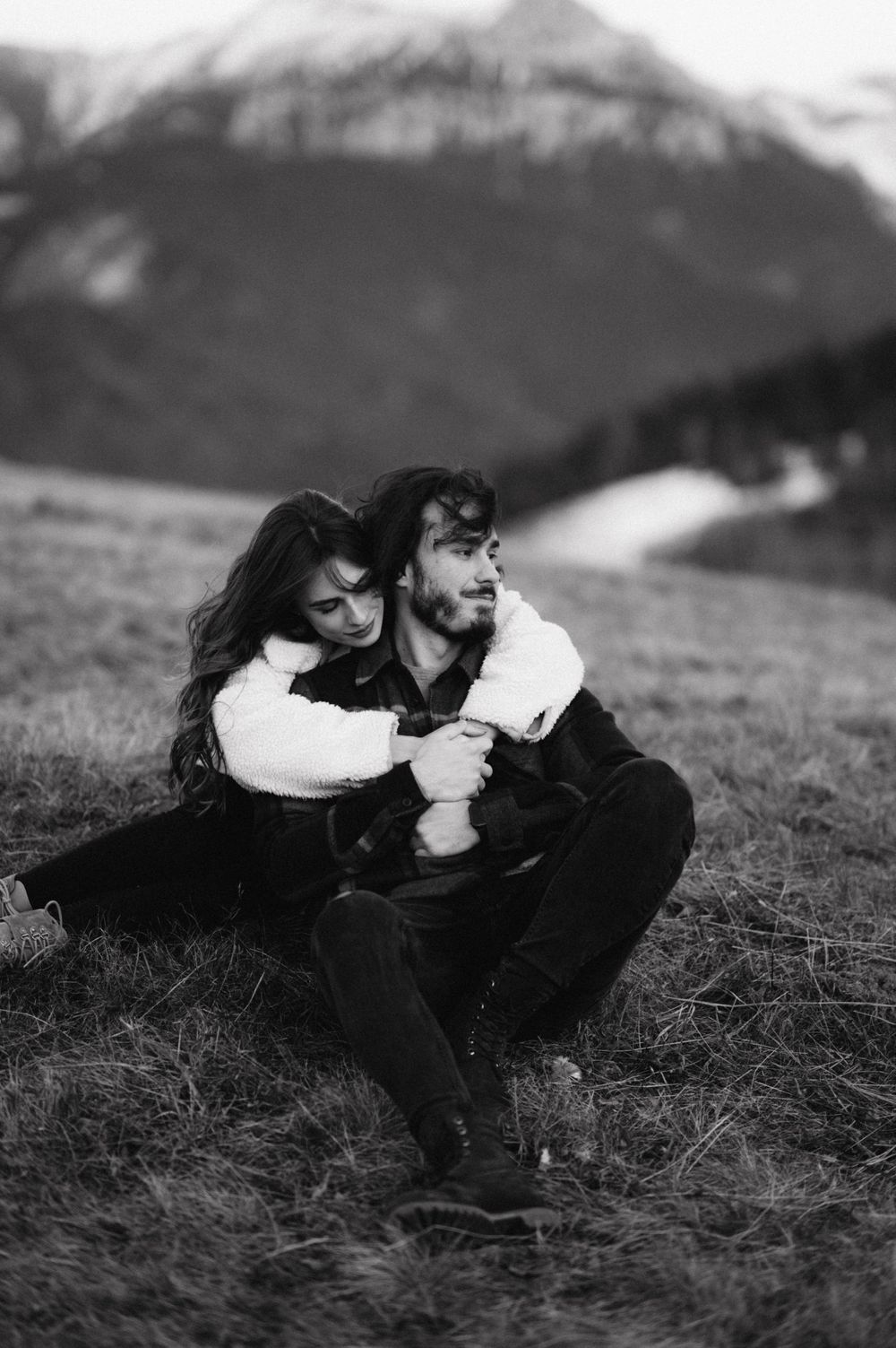 A black and white portrait of a couple sharing an intimate moment in a mountain setting.