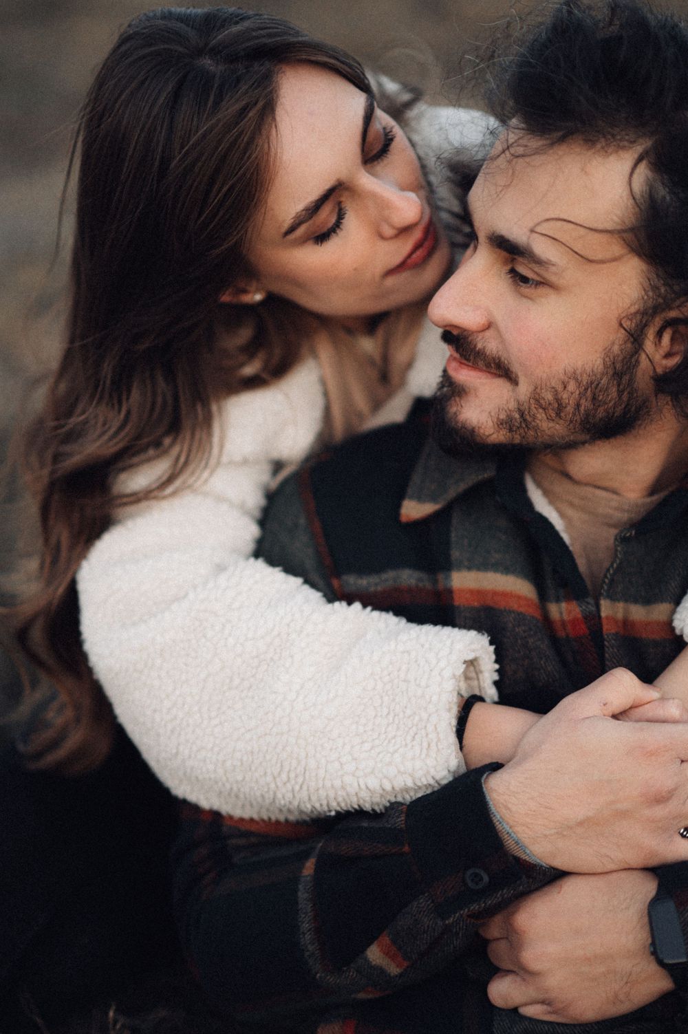 Intimate couple sharing tender moment in cozy winter wear with soft natural lighting.