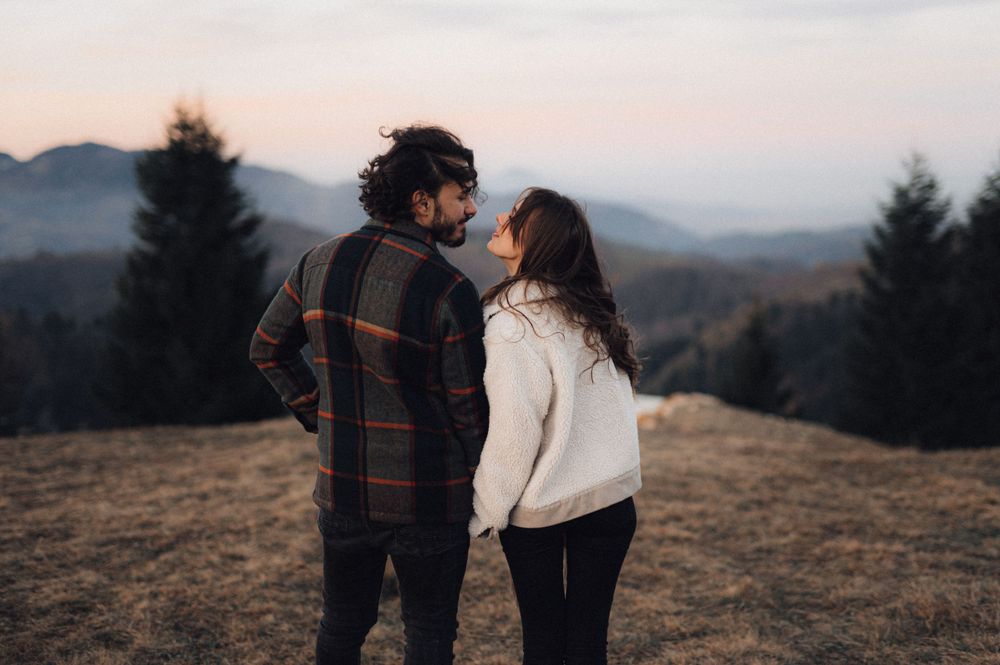 A couple shares an intimate moment against a misty mountain landscape at sunset.
