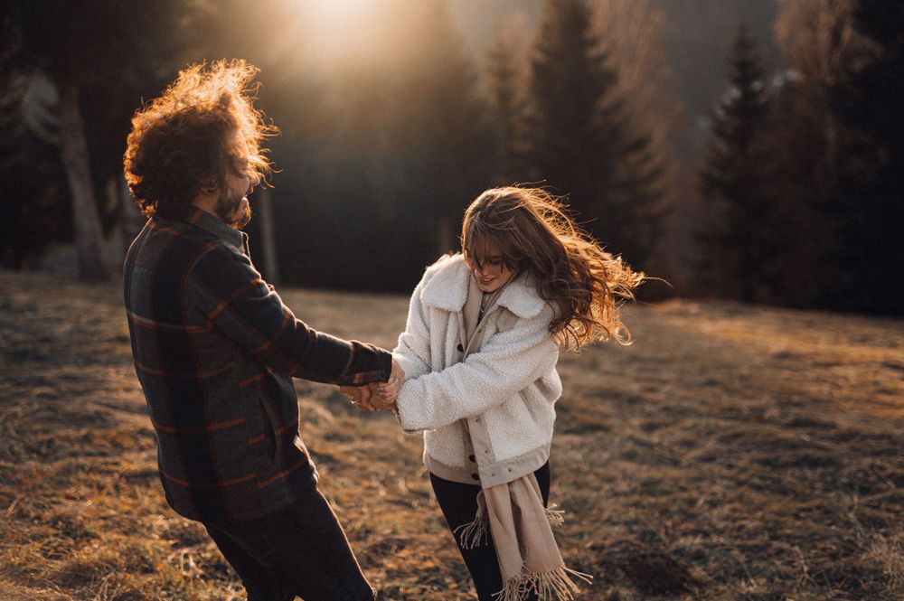 Two people dancing energetically on a hilltop with their hair flowing in the wind at sunset.