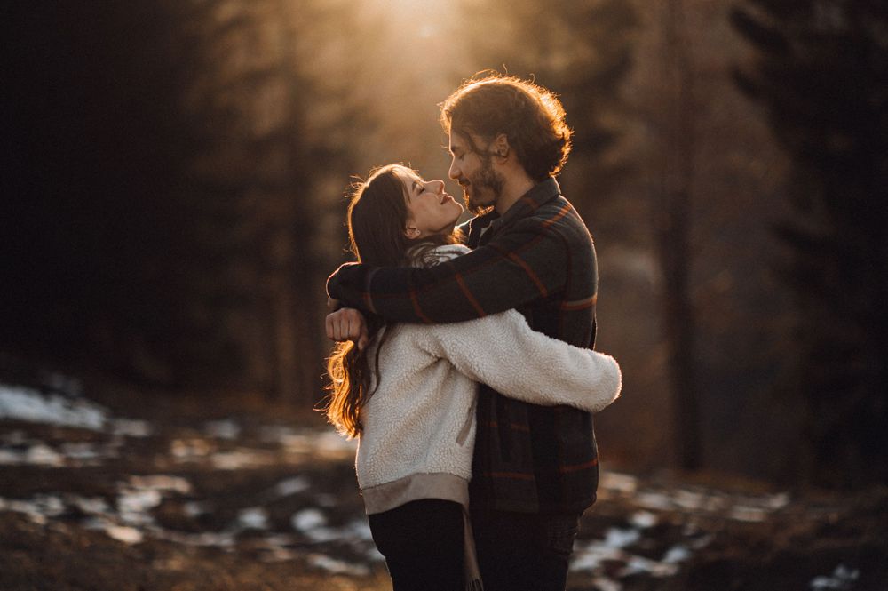 Joyful winter embrace captured against golden sunlight and snowy landscape.