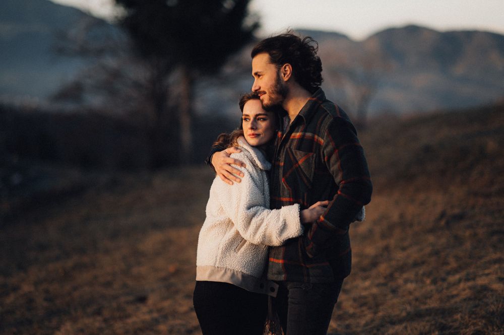 A couple embracing while standing on a mountain slope during a moody sunset.