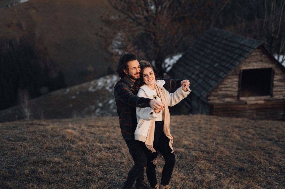Dancing couple in casual winter clothing sharing a playful moment on a hillside.