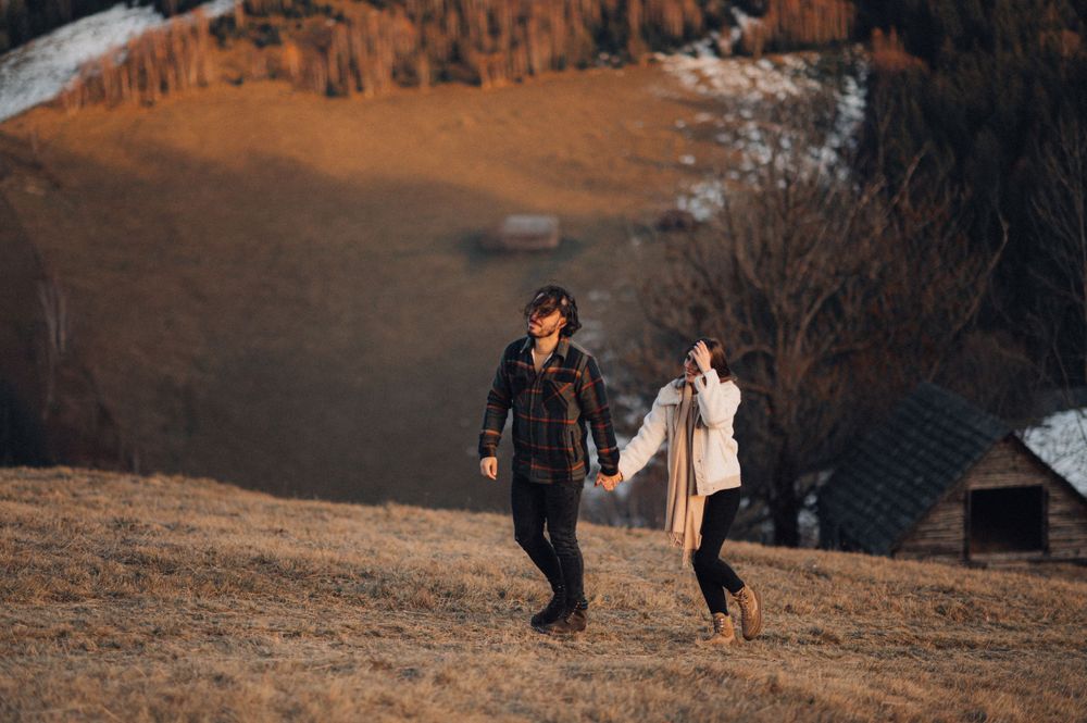 A couple walks hand in hand across a mountain meadow at sunset.