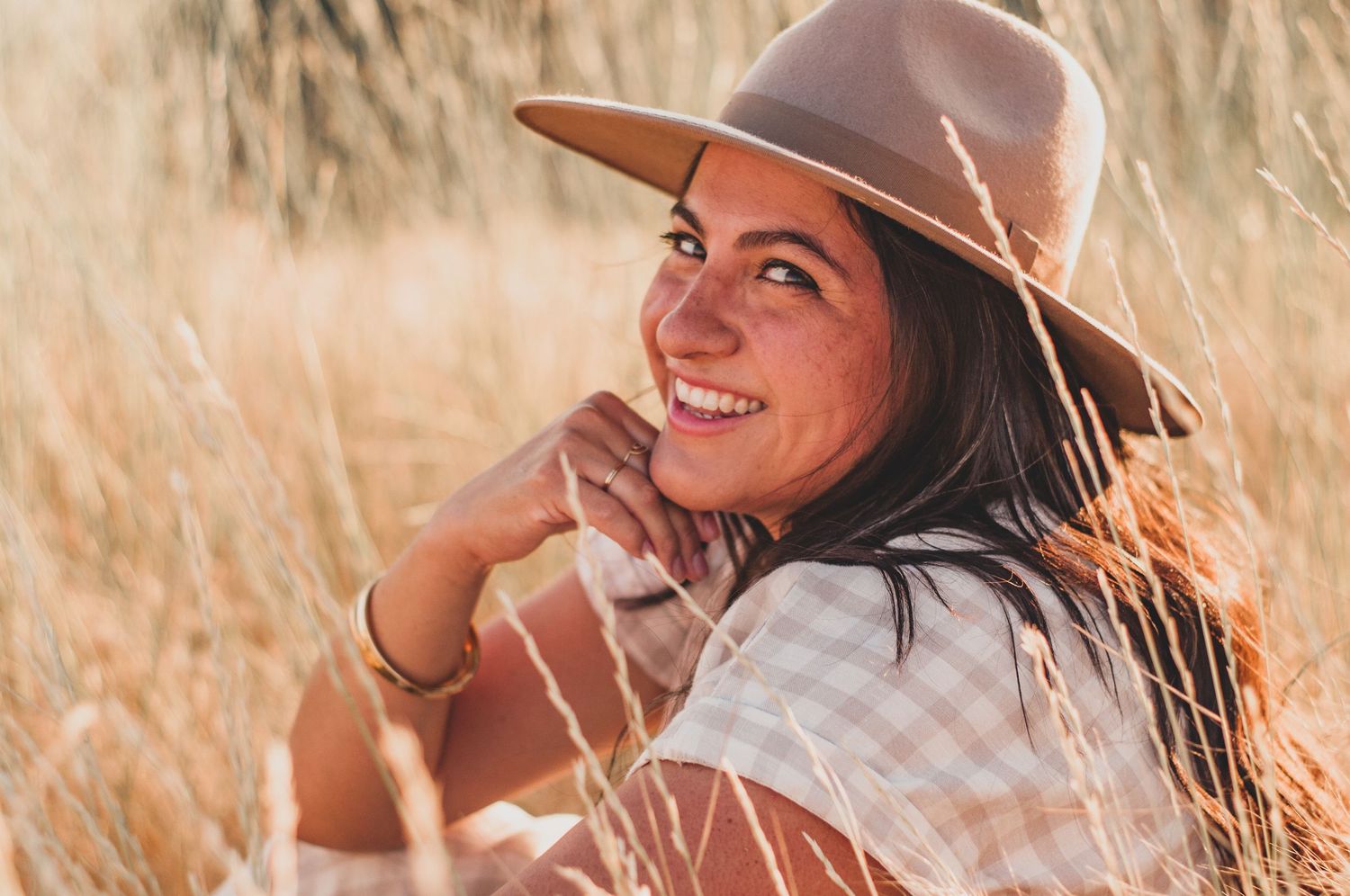 Woman wearing a hat smiling at camera in a field of wheat during a branding shoot