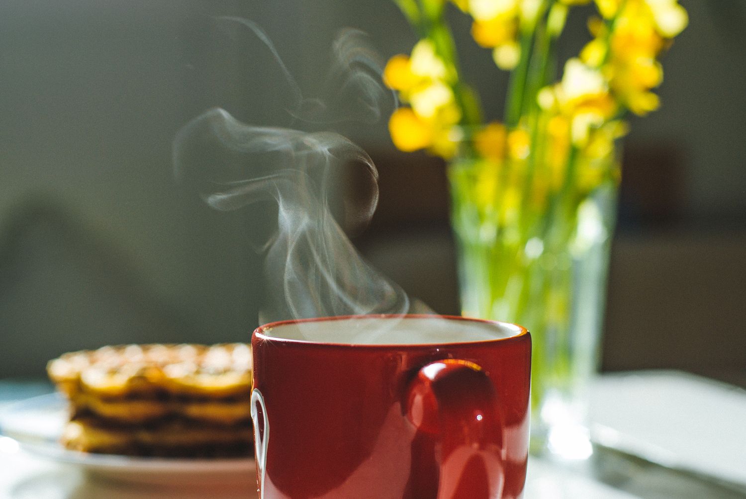 Rykende fersk kopp med kaffe, nystekte vafler og påskeliljer på spisebordet.